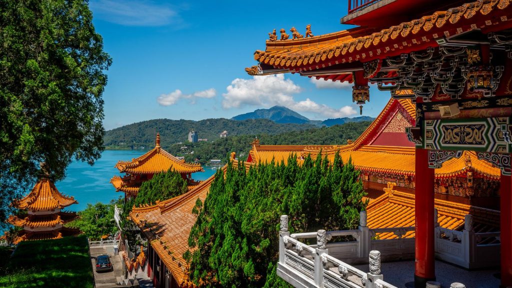 A sunny view of Sun Moon Lake in Taiwan from a beautiful Wen Wu temple along the shore of the lake, highlighting its distinctive orange-red tiled roofs.